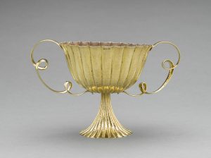 Shiny fluted golden goblet with a curved lip and two handles curled like ribbons.