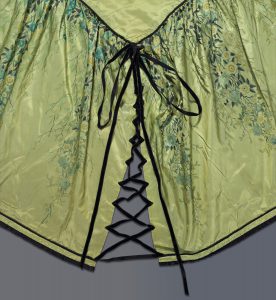 A close-up of the bedcover showing black velvet ribbon corseted at one of the corners.