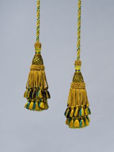 A pair of greenish-yellow curtain ties with blue, yellow, and black fringes.