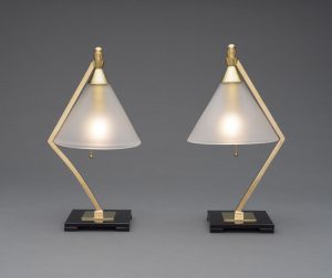 Two desk lamps with brass, skinny, angled stems, triangular frosted glass shades, and square black glass bases.