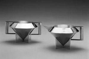 A silver sugar bowl and a silver cream pitcher composed of bold triangular and rectangular forms.