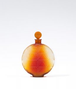 A circular glass bottle with orange ombré coloring and a triangular pattern cut on its surface. Bottle stopper is a flat orange circle.
