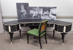 A curved dressing table and chair, with enlarged archival photos of Elaine Wormser’s bedroom sitting on the table.
