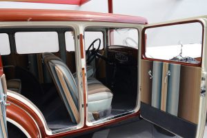 Color photo of the passenger side of a mahogany brown Ruxton automobile with the front and back doors open. The seats and the inside of the car door are covered in blue, yellow, and brown striped upholstery.