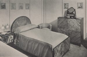 Black and white photo of a bedroom with a glossy black table with a hollow center, containing a shelf, and white detailing around the edges.