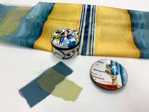 Striped yellow, green, and blue fabric samples next to a colorful lidded box and dish.