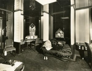 Black and white photo of an interior showing two chairs with curved backs, dark upholstery, and shiny frames. The chairs’ structure resembles the ones in the Wormser bedroom.