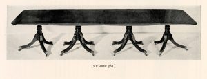 A long, dark table with four sets of splayed legs.