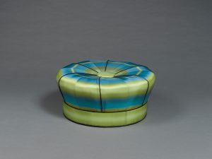 A round ottoman upholstered in blue and green ombré fabric.