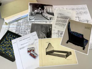 Documents with images of furniture, blueprints, and archival photos of the room laid out on a table.