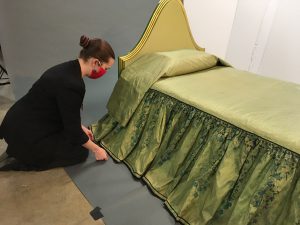 Woman adjusts the skirt of Elaine Wormser’s bedspread as it drapes over the bed.