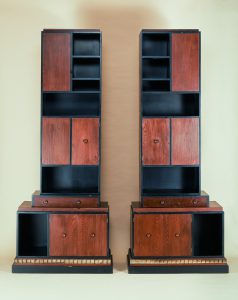 Two bookcases in brown and black wood, composed of rectangular forms of different sizes.