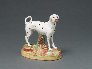 A ceramic dalmatian standing on a green and brown oval.