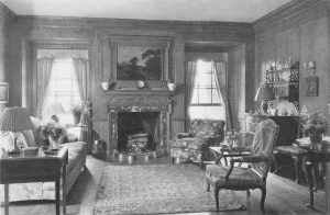 A living room decorated with eighteenth-century Georgian style furniture, with wood paneling on the walls and a large floral rug on the floor.