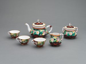 Ceramic tea set decorated with colorful floral motifs on a white background. Set includes a teapot, cream pitcher, double-handled sugar bowl and three teacups.