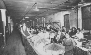 Young Black women seated at long tables, many with bobbed hair, looking down as they stitch lampshades.